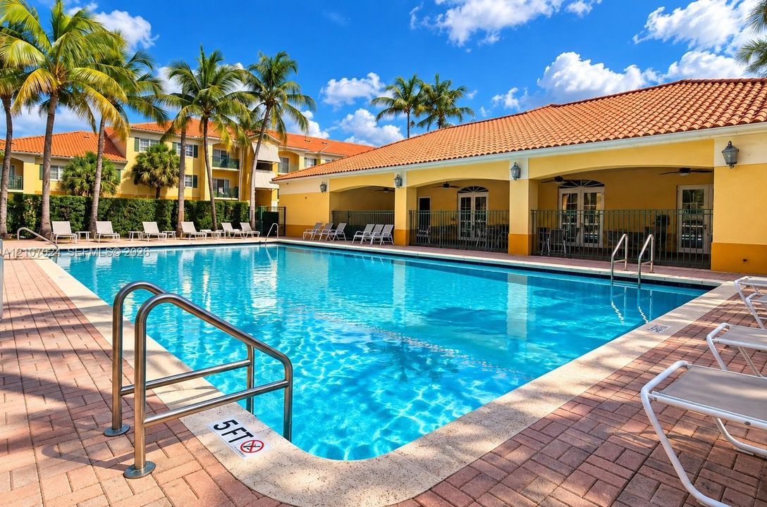 In-ground swimming pool featuring a brick paver deck, stainless steel handrails, and a covered patio area with archway details and tile roofing