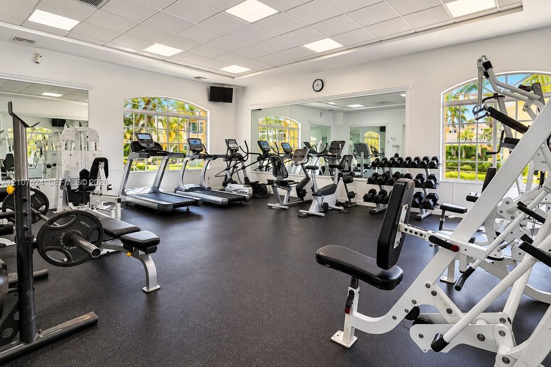 Fitness center featuring rubberized flooring, expansive wall-to-wall mirrors, recessed grid ceiling lighting, and large arched windows