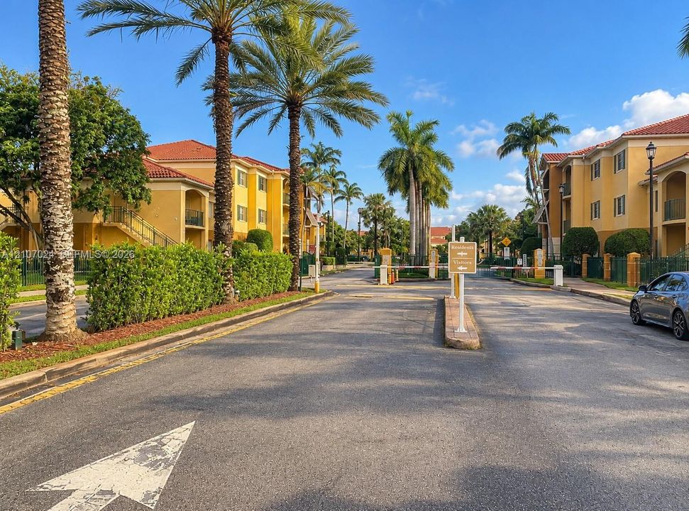 Gated residential entrance featuring terracotta-tiled roof buildings, stucco exterior facades, and manicured palm tree landscaping