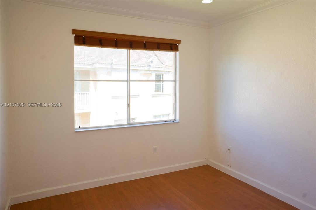 Interior room featuring wood-finish flooring, white wall surfaces, crown molding, and a sliding window with a horizontal blind