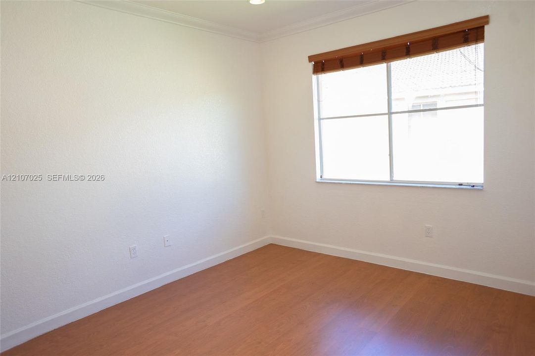 Neutral-toned room featuring wood-finish flooring, textured walls, and a large window equipped with an integrated wood-slat blind