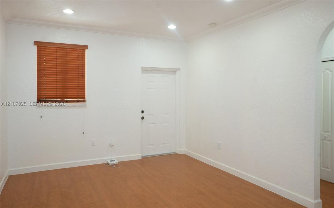 Interior room featuring wood-finish flooring, recessed lighting, crown molding, an arched entryway, and a window with horizontal blinds