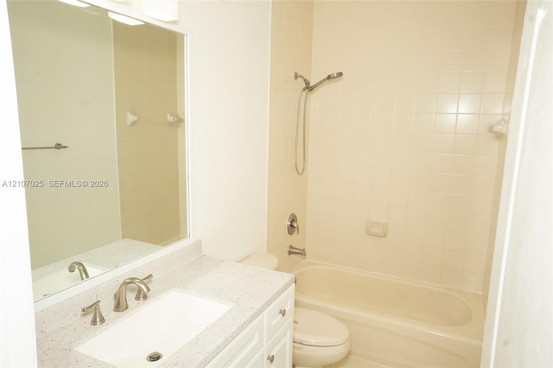 Bathroom vanity with a stone-finish countertop, undermount sink, brushed-nickel faucet, large wall mirror, and a tub-shower combination with tile surround