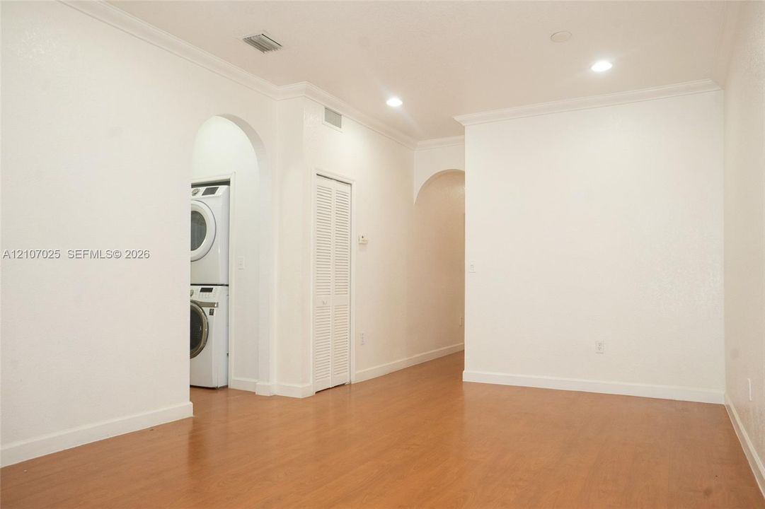 Interior space featuring wood-finish flooring, recessed lighting, crown molding, arched entryways, and a dedicated laundry area with stacked appliances