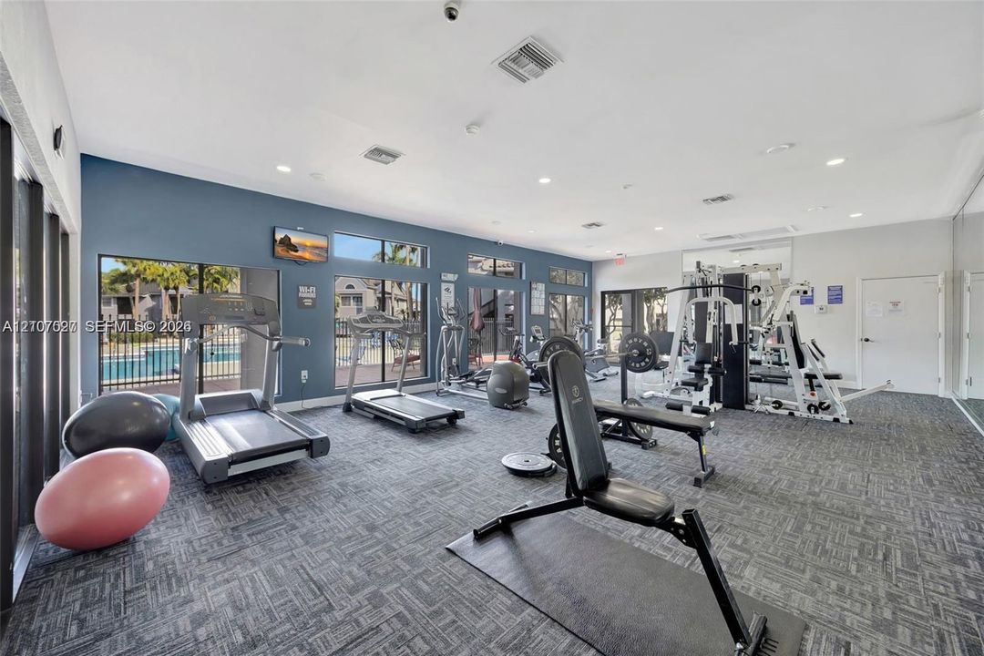 Fitness center featuring expansive floor-to-ceiling windows, high-contrast wall finishes, patterned carpet tiles, and recessed lighting