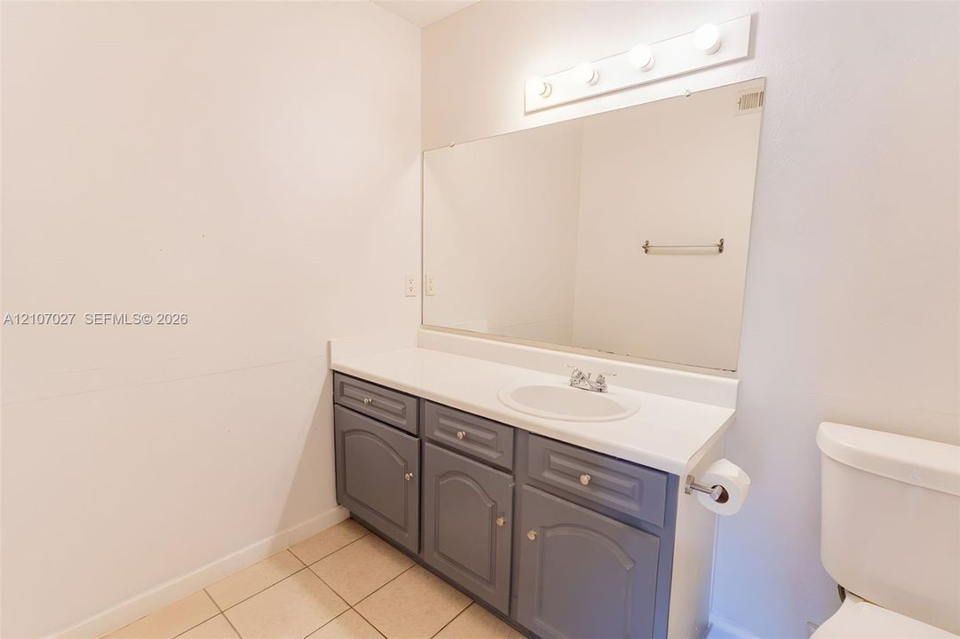 Vanity featuring a solid-surface countertop, integrated basin with a chrome faucet, gray cabinetry, wall-mounted mirror, and a multi-light fixture