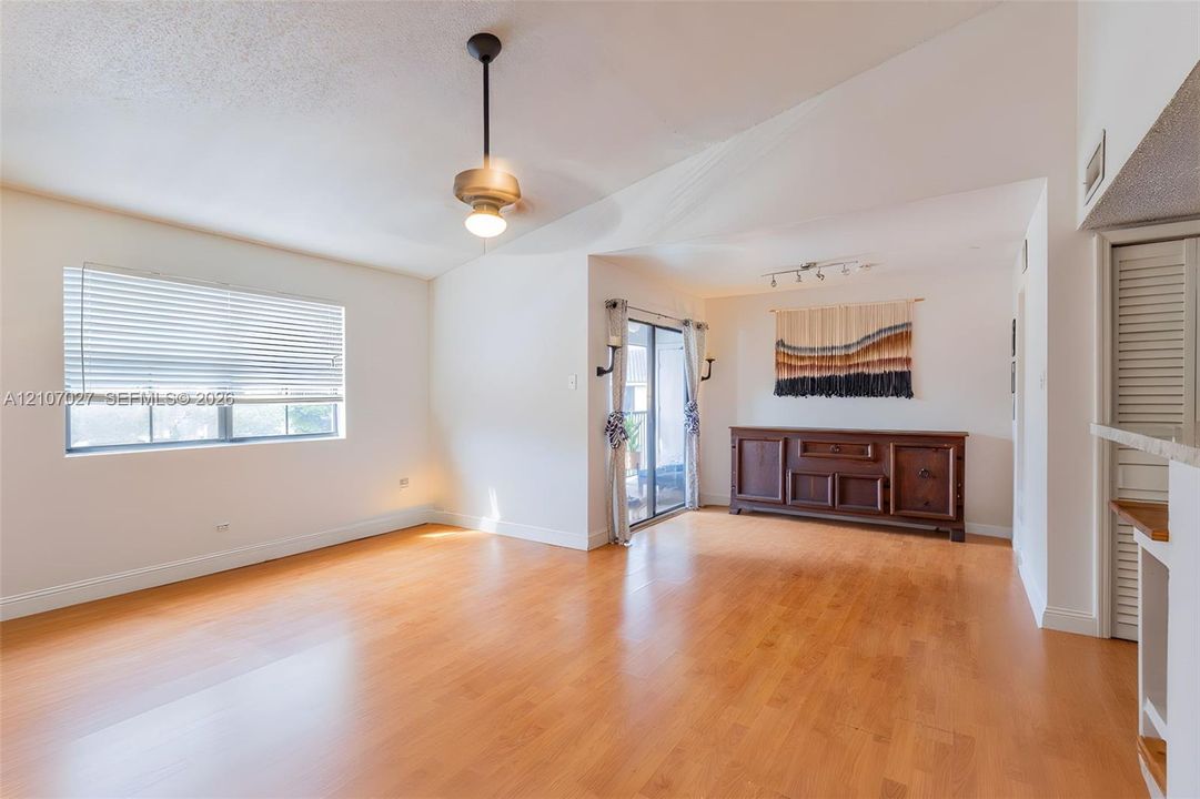 Living area featuring vaulted ceilings, wood-finish flooring, sliding glass patio doors, and a metal downrod pendant light fixture