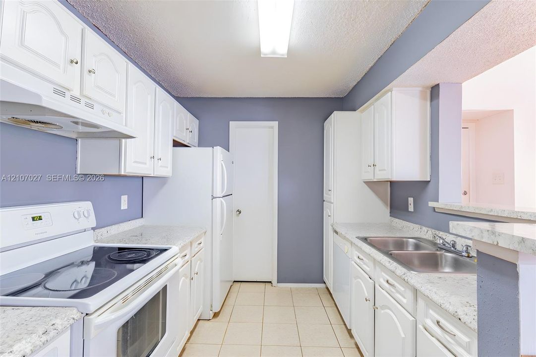 Kitchen featuring white cabinetry, light-toned stone-finish countertops, stainless steel dual-basin sink, and tile flooring