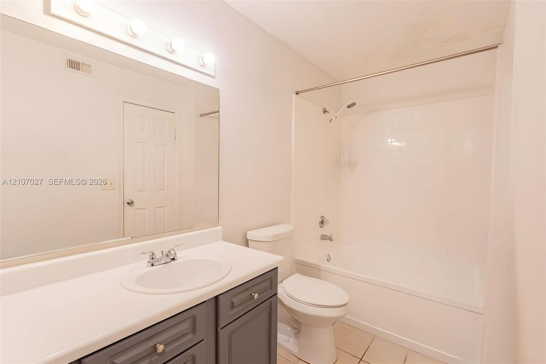 Bathroom featuring a grey vanity with a white countertop, an integrated oval sink, a full-width mirror, a wall-mounted light fixture, and a tub-shower combination with tile surround