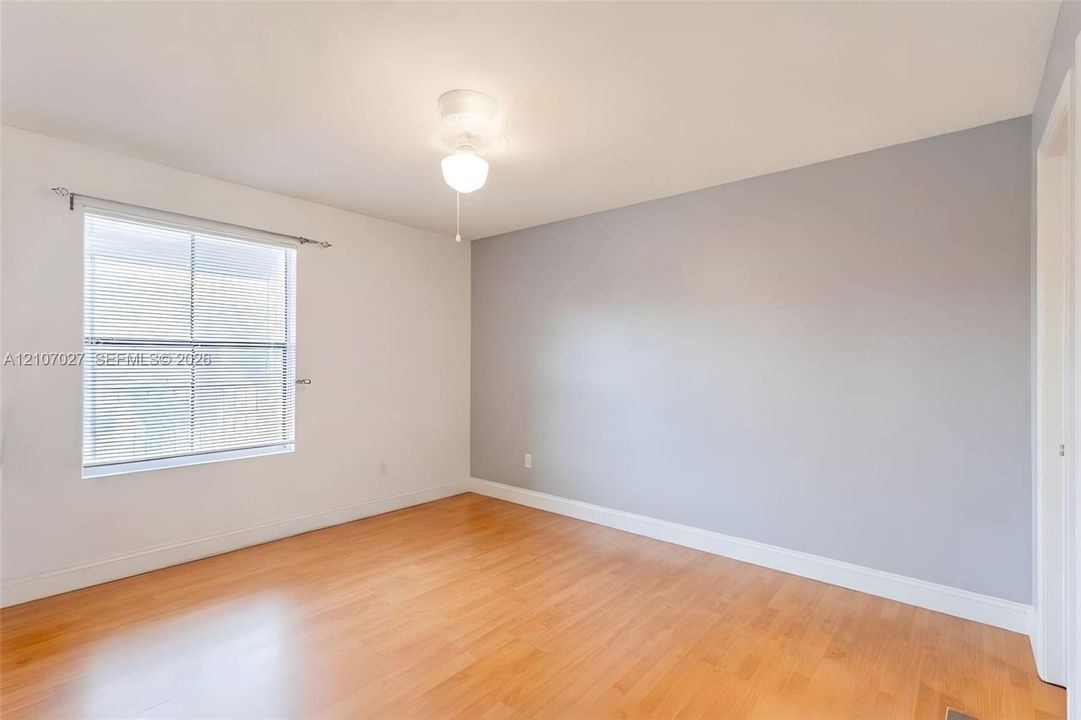 Neutral-toned room featuring wood-finish flooring, a single-pane window with horizontal blinds, and a central ceiling light fixture
