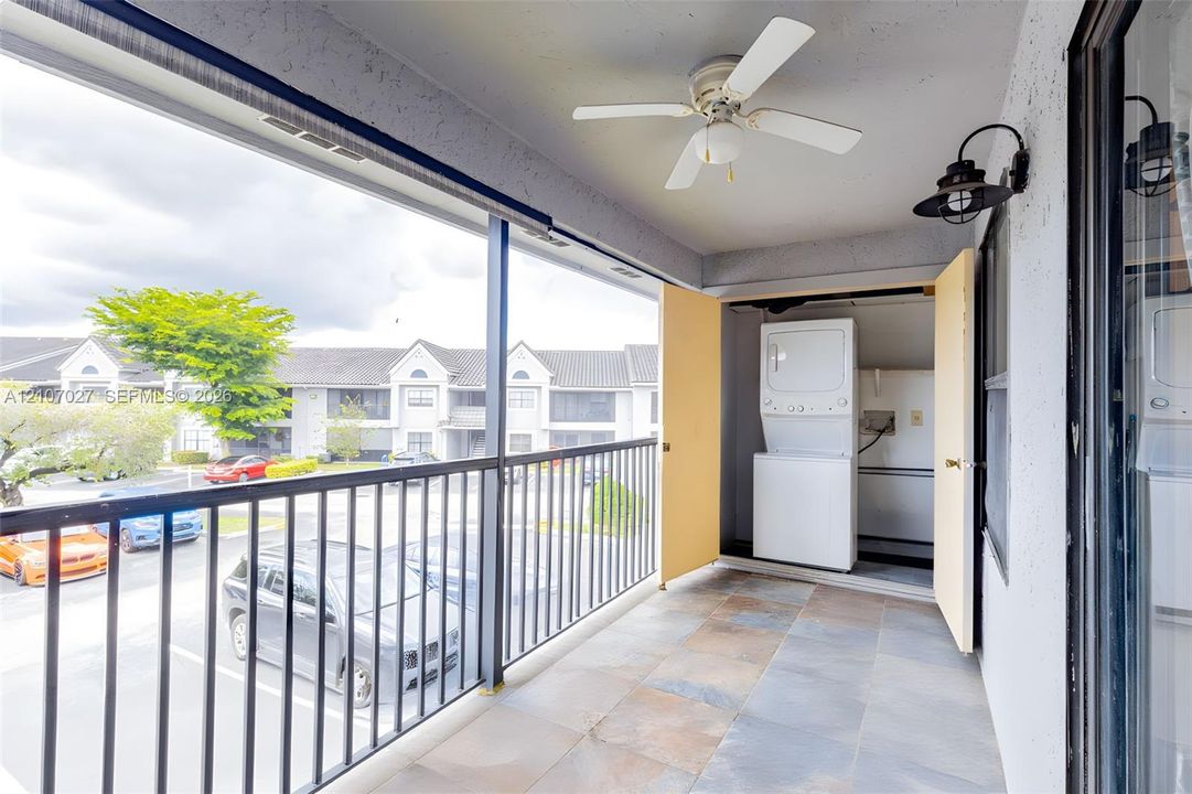 Covered balcony featuring tile flooring, a ceiling fan, black metal railing, and a built-in laundry closet with a stacked washer and dryer