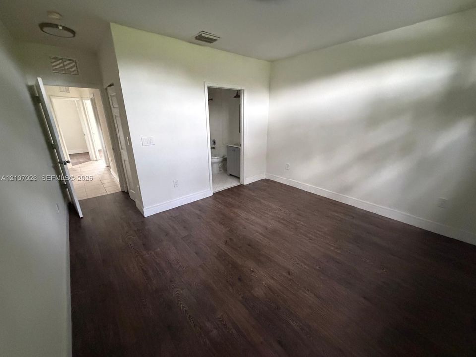 Interior room featuring wood-finish flooring, white walls, and a dedicated doorway providing entry to a secondary space with a vanity and tile flooring