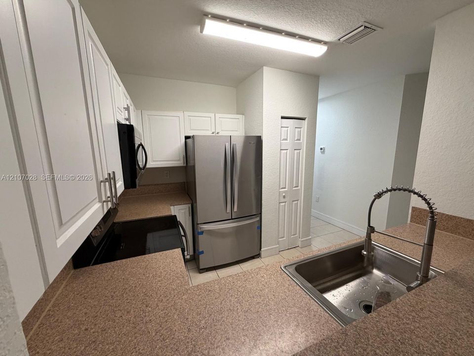 Kitchen featuring white shaker-style cabinetry, stainless steel French-door refrigerator, solid surface countertops, a high-arc pull-down kitchen faucet, and a dual-panel interior closet door