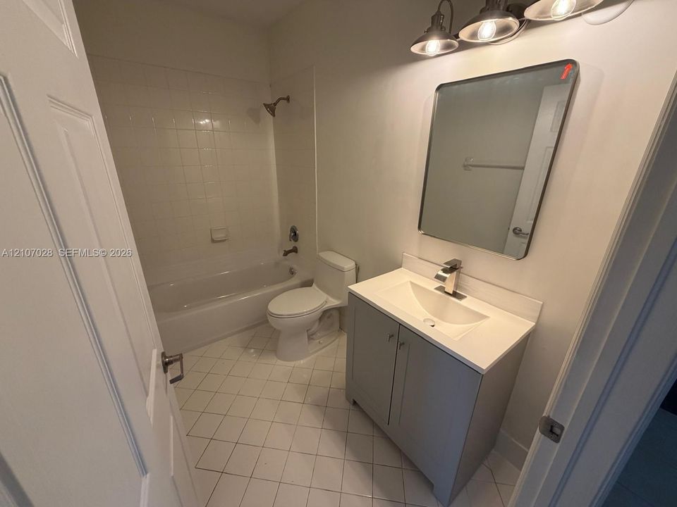 Bathroom featuring a vanity with a solid-surface countertop and integrated sink, a rectangular wall-mounted mirror, a three-light fixture, and a tub-shower combination with tile surround