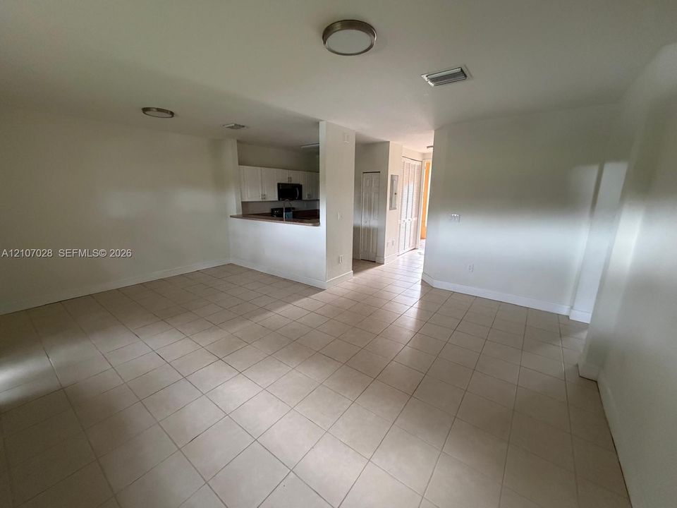 Open-concept interior featuring neutral tile flooring, recessed ceiling lighting, a pass-through kitchen counter, and crisp white cabinetry