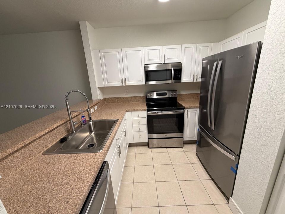 Kitchen featuring white shaker-style cabinetry, solid-surface countertops, stainless steel appliances, a pull-down kitchen faucet, and tile flooring
