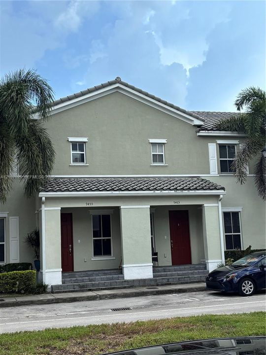 Two-story exterior featuring a neutral stucco facade, a tiled roof, covered ground-level porches, and contrasting trim accents