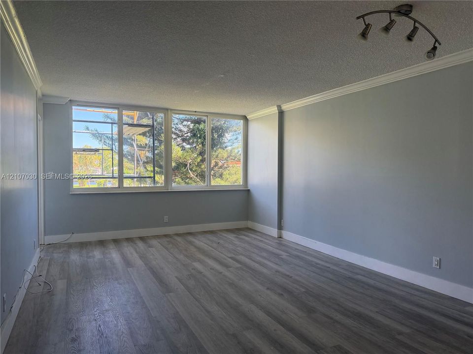Open-concept living space featuring wood-finish flooring, crown molding, multi-pane windows, and a multi-directional track lighting fixture