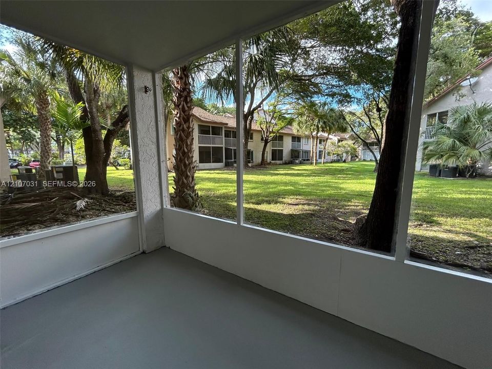 Screened-in porch featuring a painted concrete floor and white frame enclosure overlooking mature trees and lawn