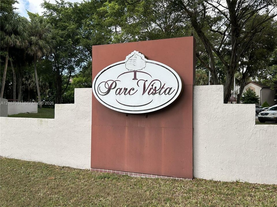 Parc Vista monument sign featuring a terracotta-finish center panel, white stucco stepped-wall masonry, and mature tree landscaping