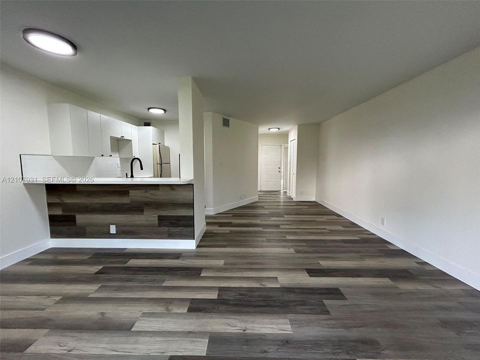 Wood-finish flooring throughout, white cabinetry, integrated kitchen peninsula with wood-accented face, matte black faucet, and flush-mount ceiling lighting