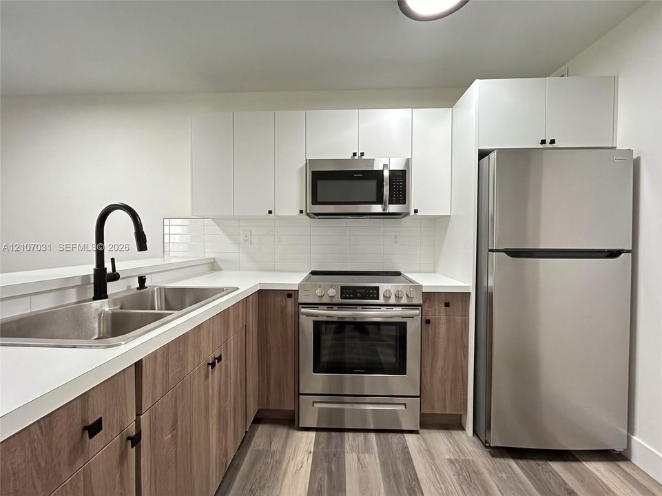 Kitchen featuring dual-tone cabinetry, stainless steel appliances, white solid-surface countertops, subway tile backsplash, and a matte black gooseneck faucet