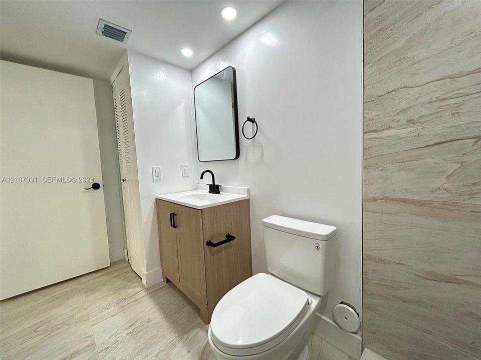 Modern vanity with wood-finish cabinetry, rectangular sink, and matte black hardware, paired with a rectangular mirror, recessed lighting, and tile wall surround
