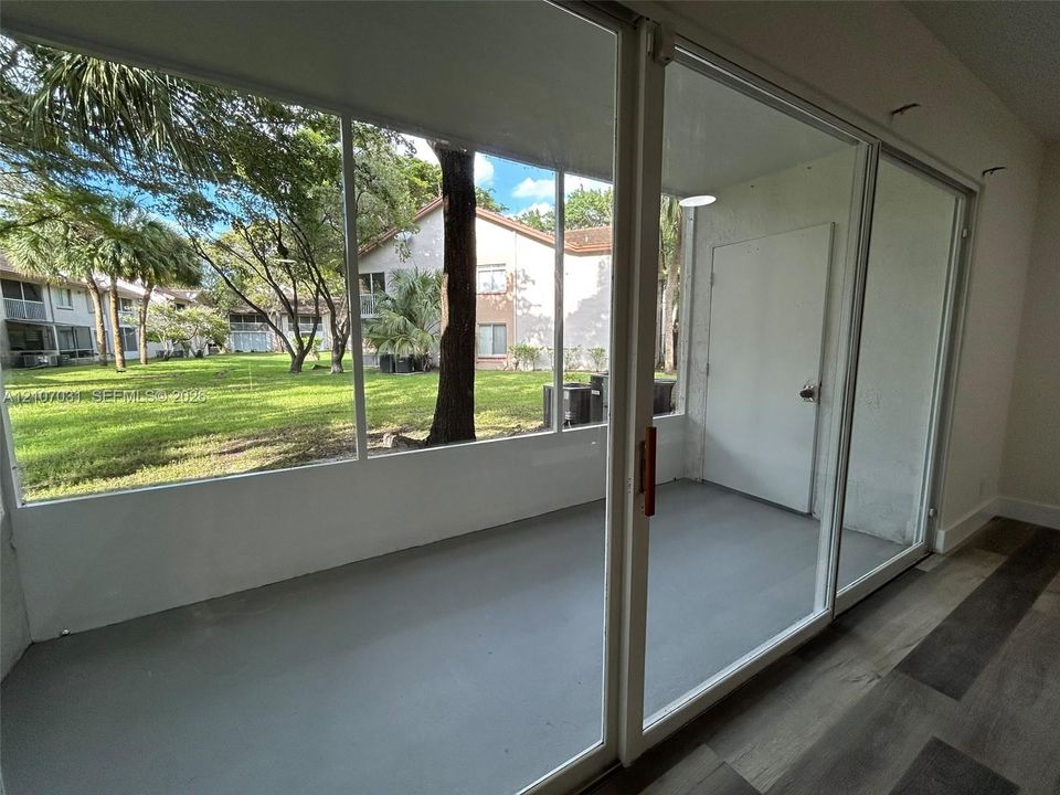 Screened-in enclosure featuring expansive glass panel walls, wood-finish flooring, and direct access to exterior green space
