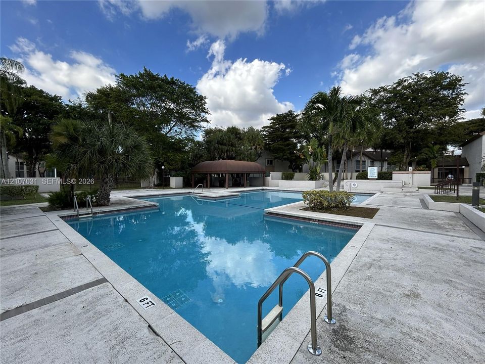 Community swimming pool featuring a concrete deck, built-in metal entry ladders, and a covered pavilion