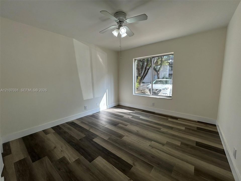 Interior room featuring wood-finish flooring, neutral walls, and a ceiling-mounted light fixture with a multi-blade fan