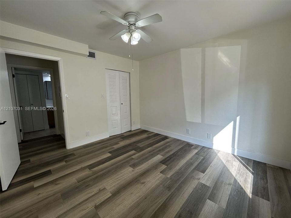 Room featuring wood-finish flooring, a ceiling fan with integrated lighting, and louvered-panel closet doors