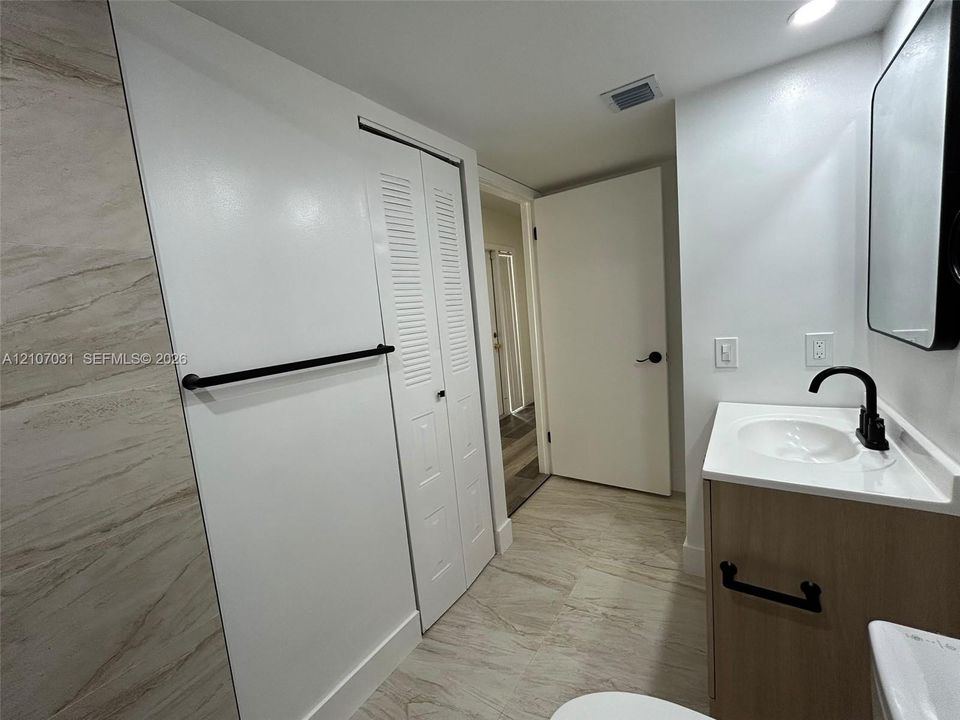 Bathroom featuring wood-finish vanity with an integrated sink, matte black faucet and hardware, tile flooring, and a louvered-panel closet door