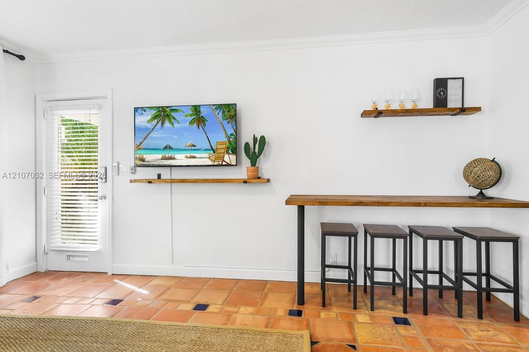 Terracotta tile flooring with inlaid decorative tiles, white interior walls, built-in wooden shelving, and a wall-mounted wooden counter with metal support legs