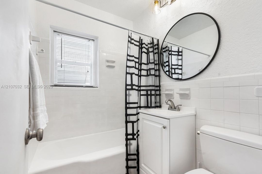 Bathroom featuring a white vanity cabinet, square wall tile surround, circular mirror with a black frame, and a tub-shower combination