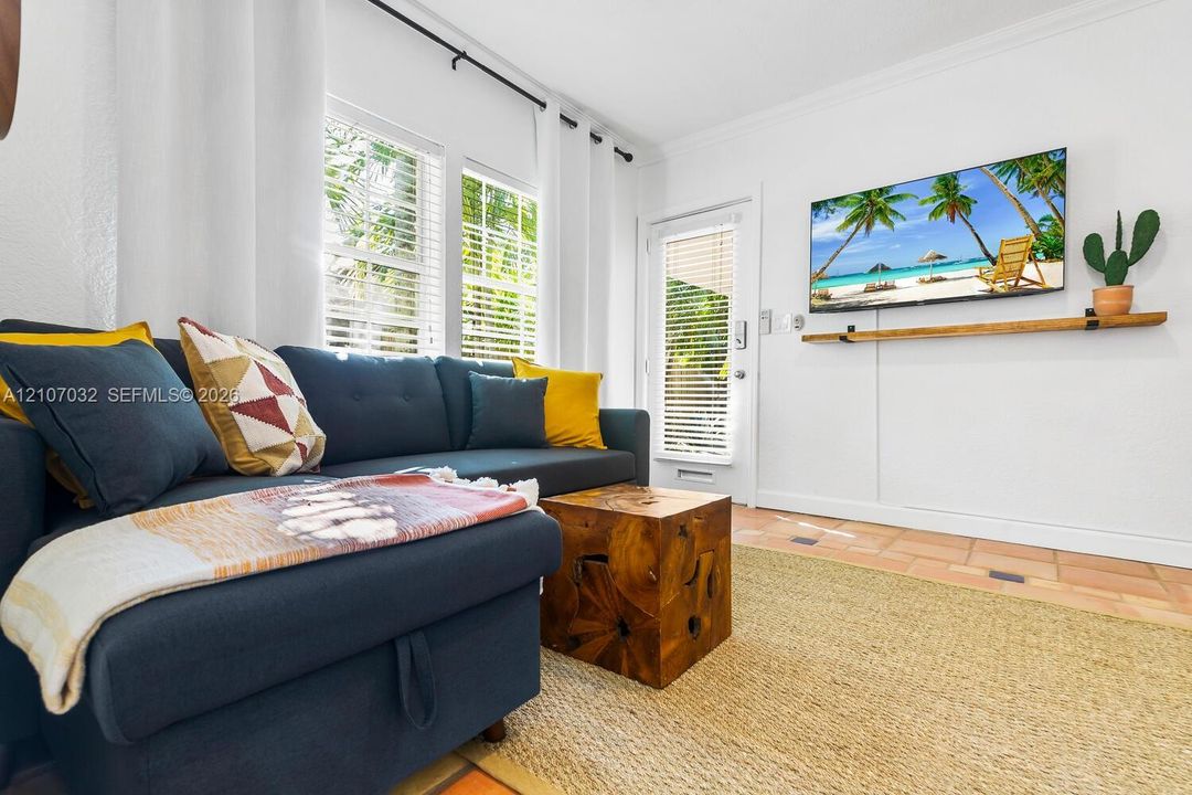 Bright living area featuring tile flooring, crown molding, double windows with blinds, and a built-in wall-mounted wooden shelf