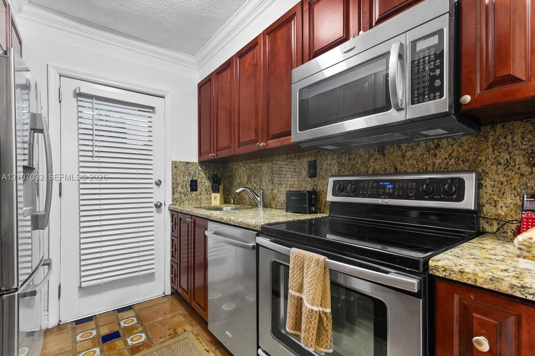 Kitchen featuring cherry-finish cabinetry, stone countertops, stainless steel appliances, and decorative tile flooring
