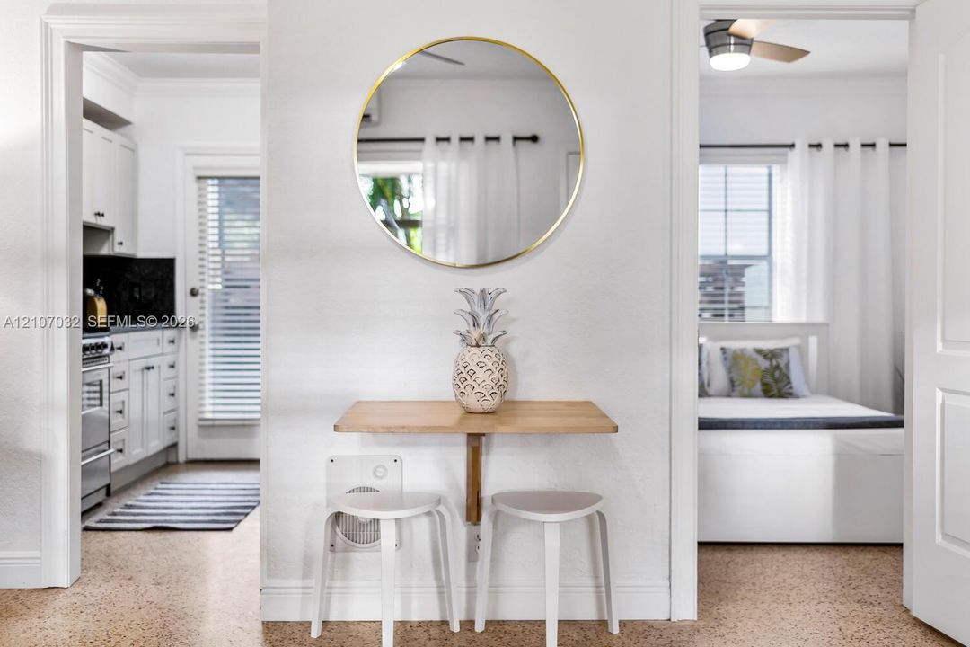 Wall-mounted wood-finish breakfast bar featuring a circular metallic-framed mirror, neutral flooring, and white cabinetry in the kitchen area