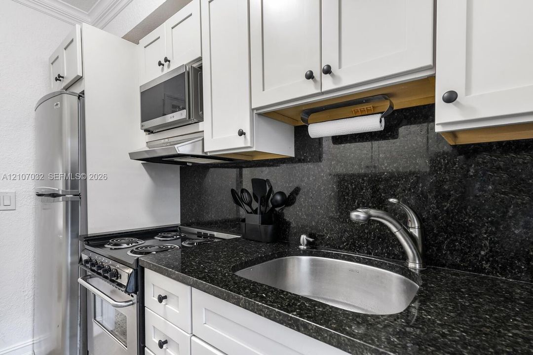 Kitchen featuring white shaker-style cabinetry, stone countertops, stainless steel appliances, and a deep-basin stainless steel sink with a high-arch faucet
