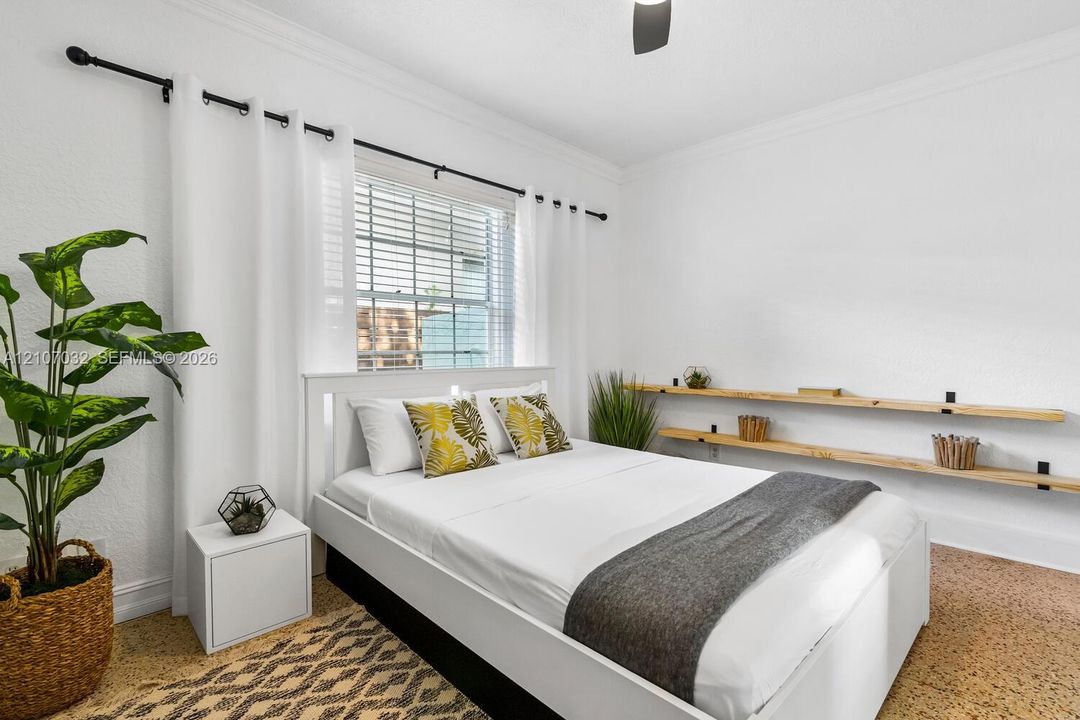 Bedroom interior featuring textured walls, crown molding, double-hung window with metal horizontal blinds, and dual natural wood-finish wall-mounted floating shelves