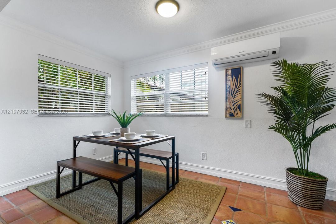 Terra-cotta tile flooring, dual windows with horizontal blinds, wall-mounted ductless climate control system, crown molding, and a flush-mount ceiling light fixture