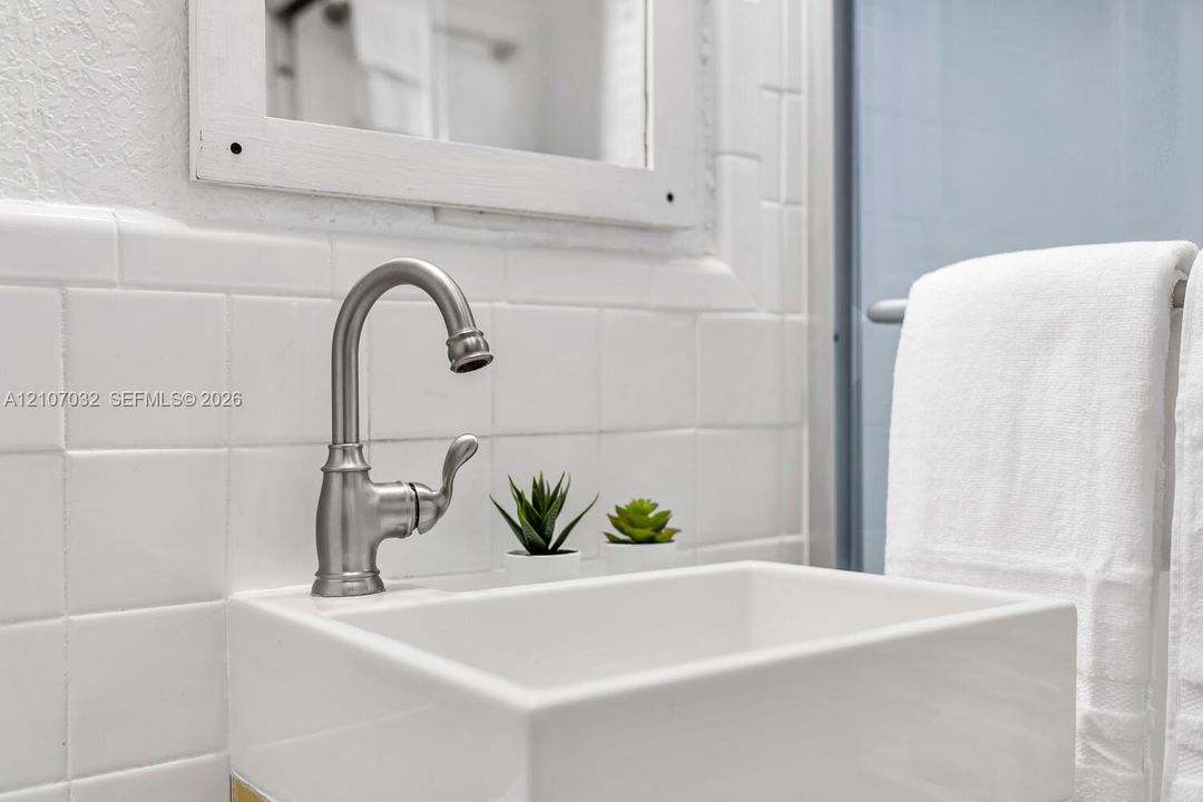 Wall-mounted square sink featuring a brushed nickel high-arc faucet and matte white tiled backsplash