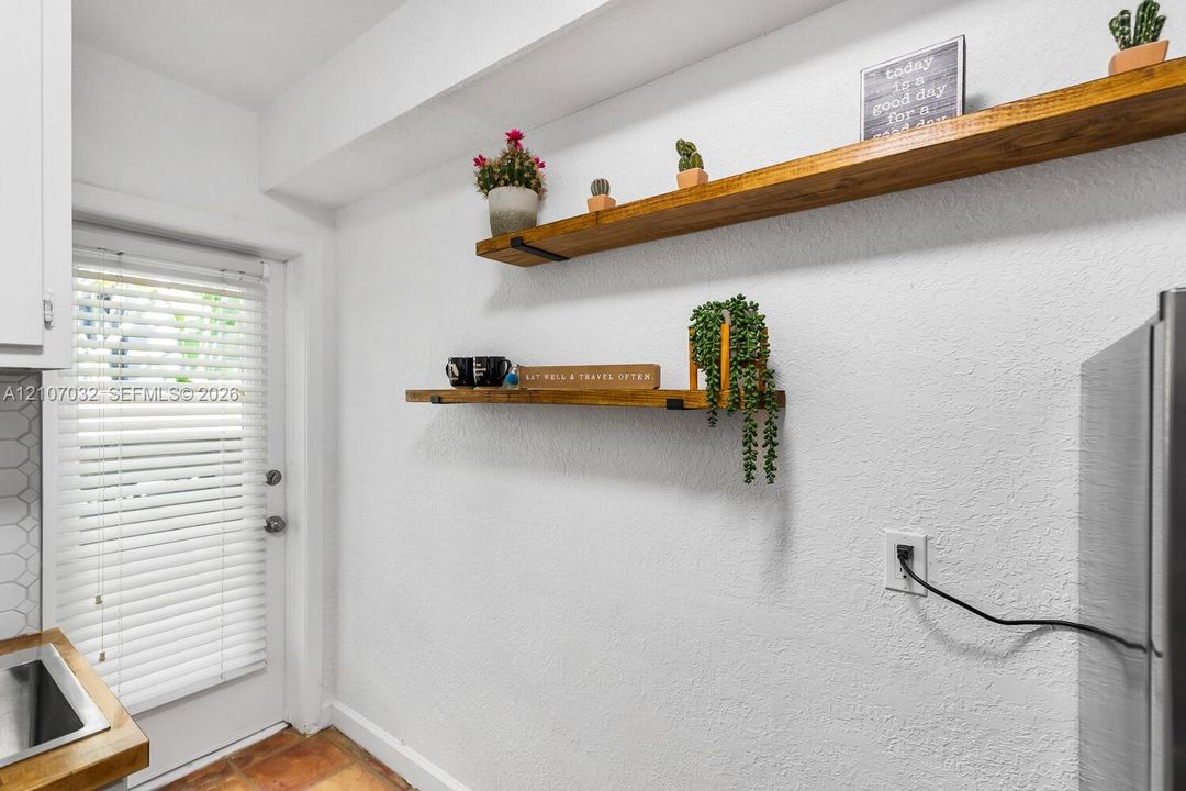 Textured walls featuring two natural wood floating shelves with matte black brackets and an exterior-access door with integrated window blinds