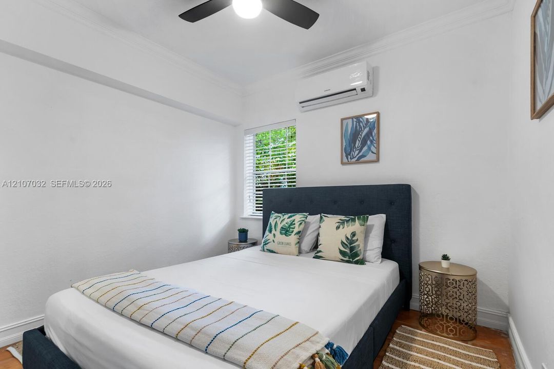 Interior space featuring wood-finish flooring, a wall-mounted ductless air conditioning unit, a multi-blade ceiling fan, and a window with white blinds