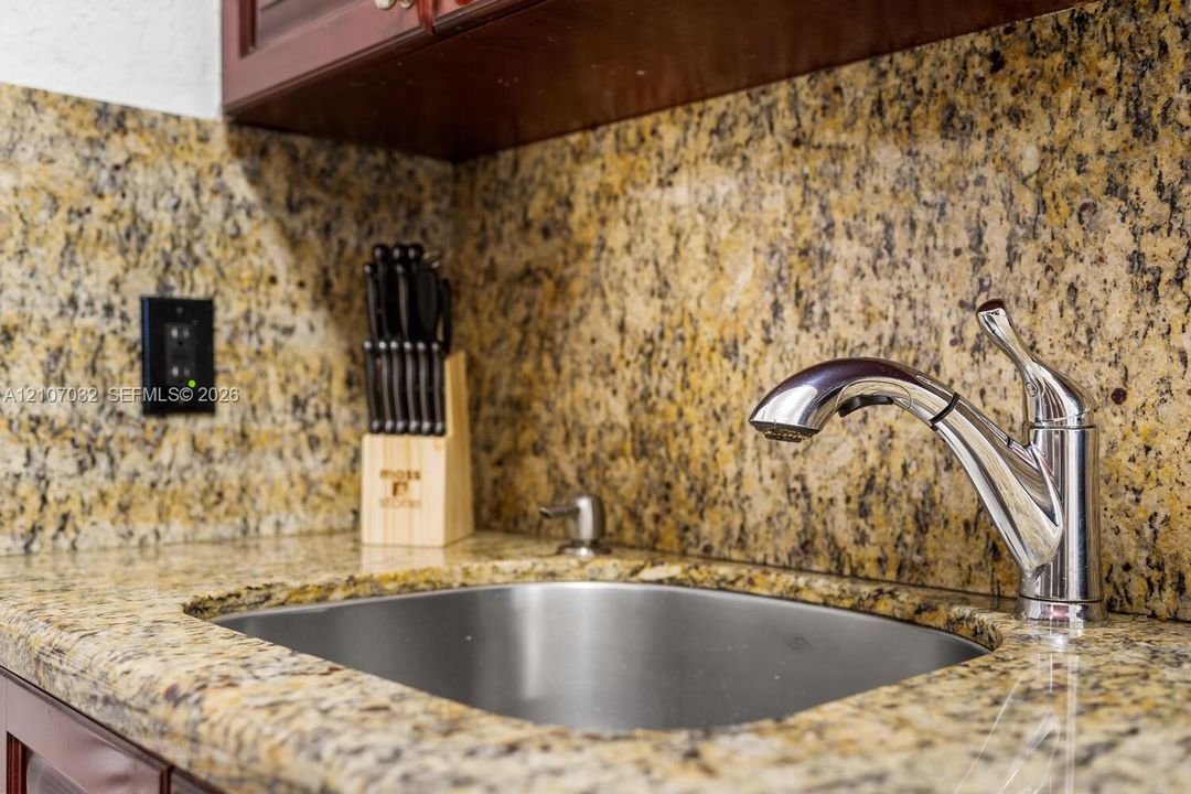 Undermount stainless steel sink featuring a chrome pull-down faucet, matching stone countertop, and full-height stone backsplash