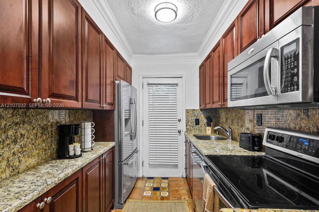 Galley kitchen featuring rich-toned wood cabinetry, stone countertops, stainless steel appliances, and tile flooring