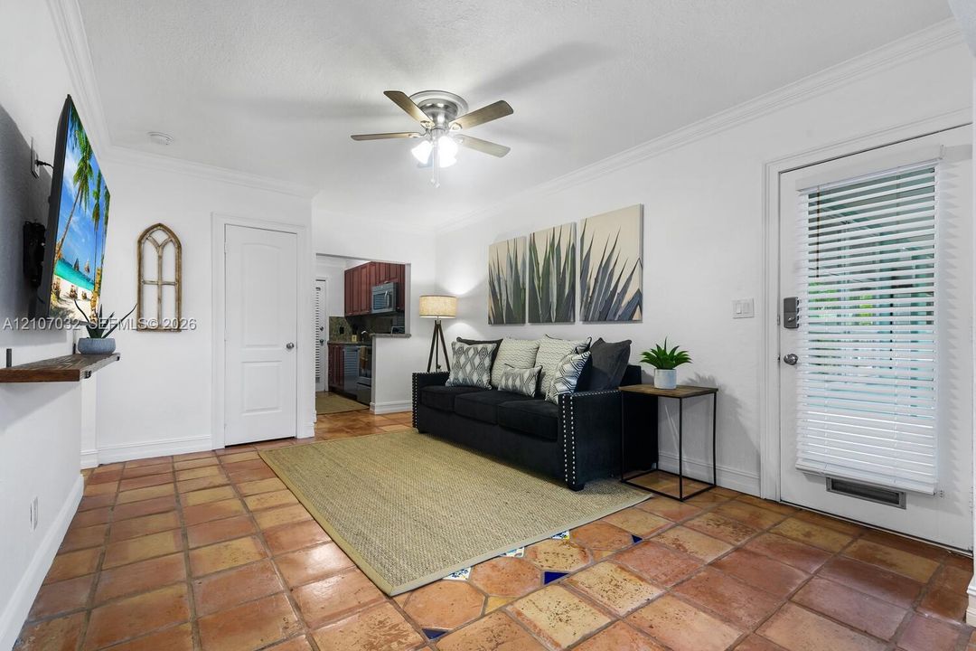 Terra-cotta tile flooring, crown molding, ceiling fan with integrated lighting, and a solid-panel interior door