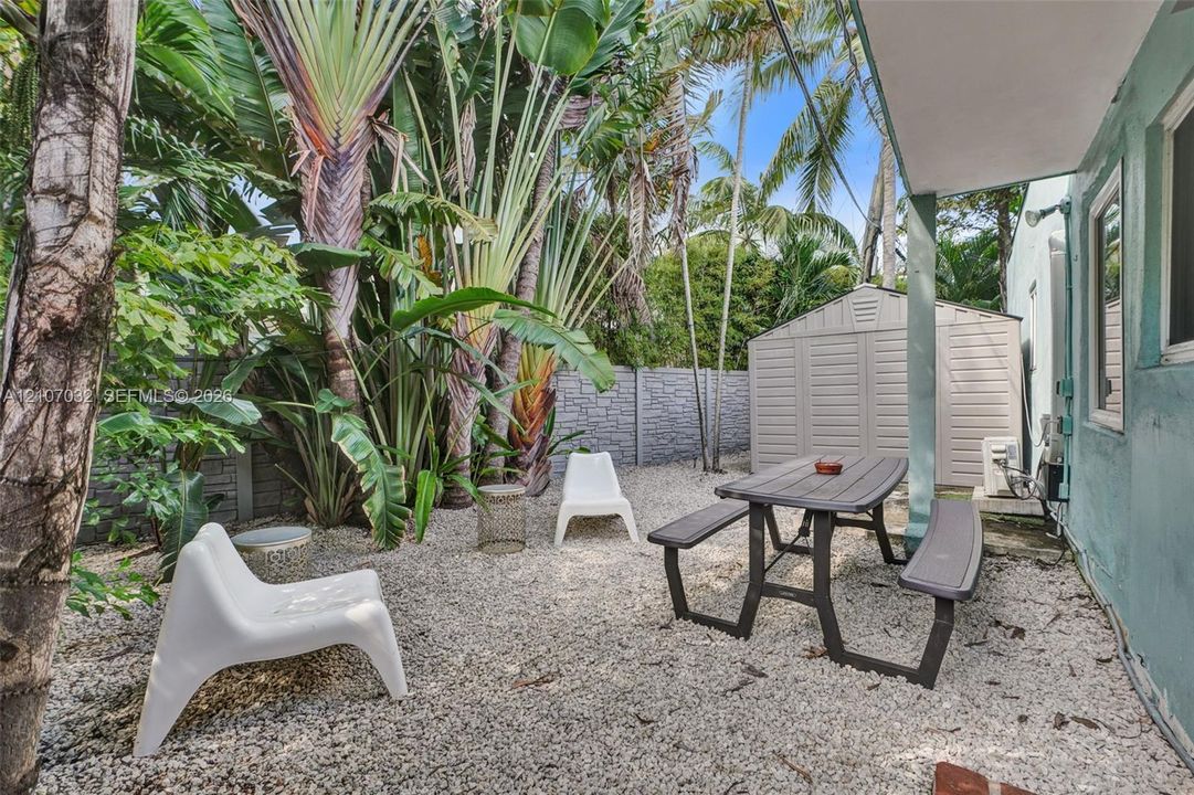 Private outdoor space featuring gravel ground cover, mature tropical landscaping, a perimeter wall, and an exterior storage structure