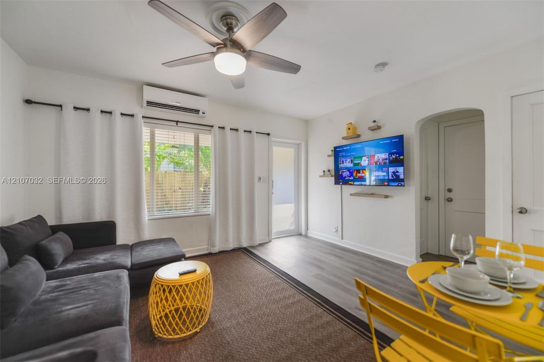 Room featuring wood-finish flooring, a wall-mounted ductless air conditioning unit, a multi-blade ceiling fan with integrated lighting, and an arched doorway