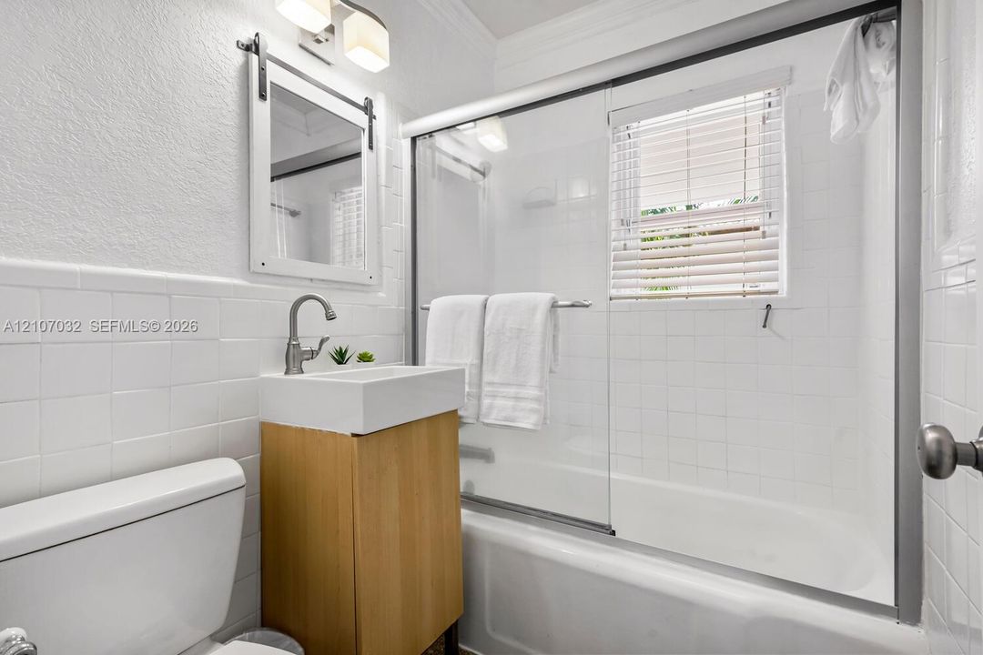 Bathroom featuring a vanity with a rectangular vessel sink, sliding glass shower doors, subway-style wall tile, a barn-door style framed mirror, and a wall-mounted light fixture