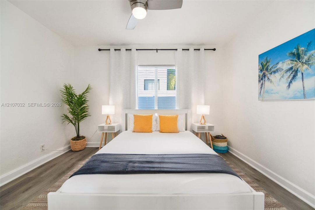 Neutral-toned interior featuring wood-finish flooring, a central ceiling fan with integrated lighting, and a window with a curtain rod fixture